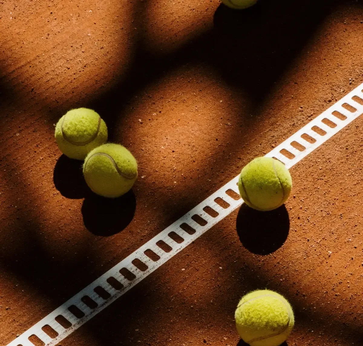 Location de raquette et de balles : des balles de tennis posées sur la ligne d'un court en terre battue