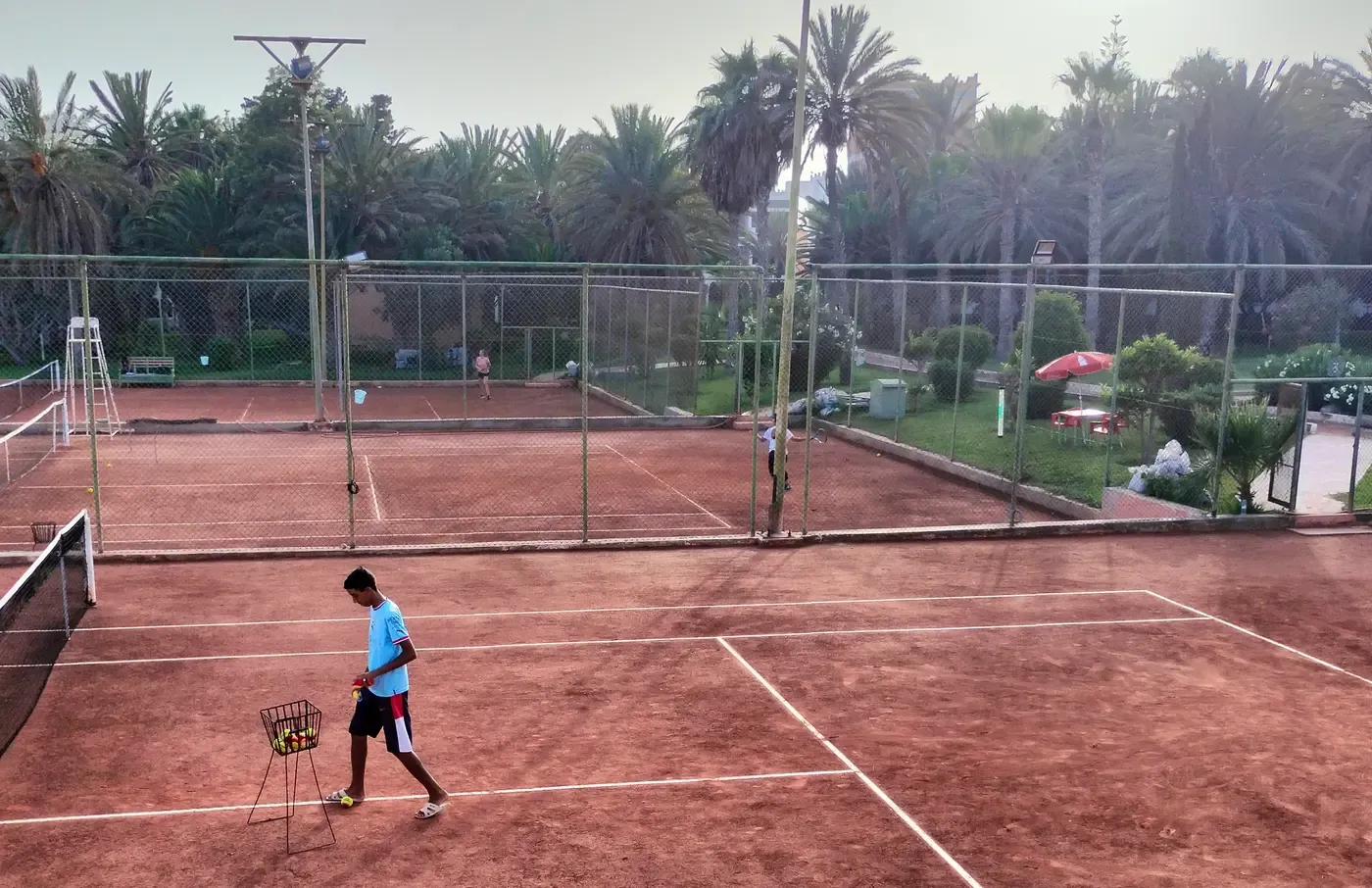 Notre approche de coaching : les courts en terre battue du club vus de loin, panier de balles en place avant une séance