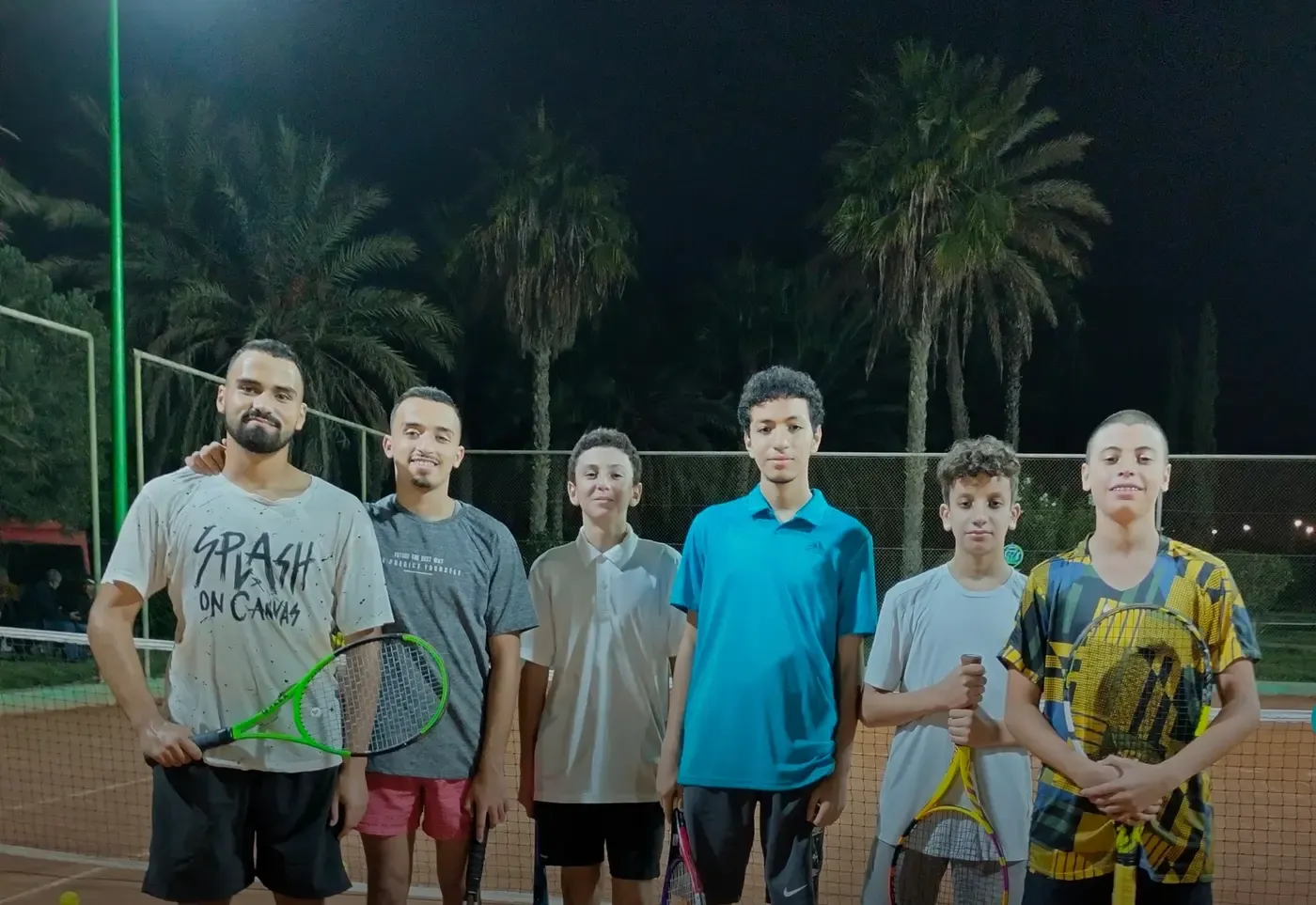 La communauté du club : le groupe de l'école réuni sur le court sous les projecteurs, raquettes à la main