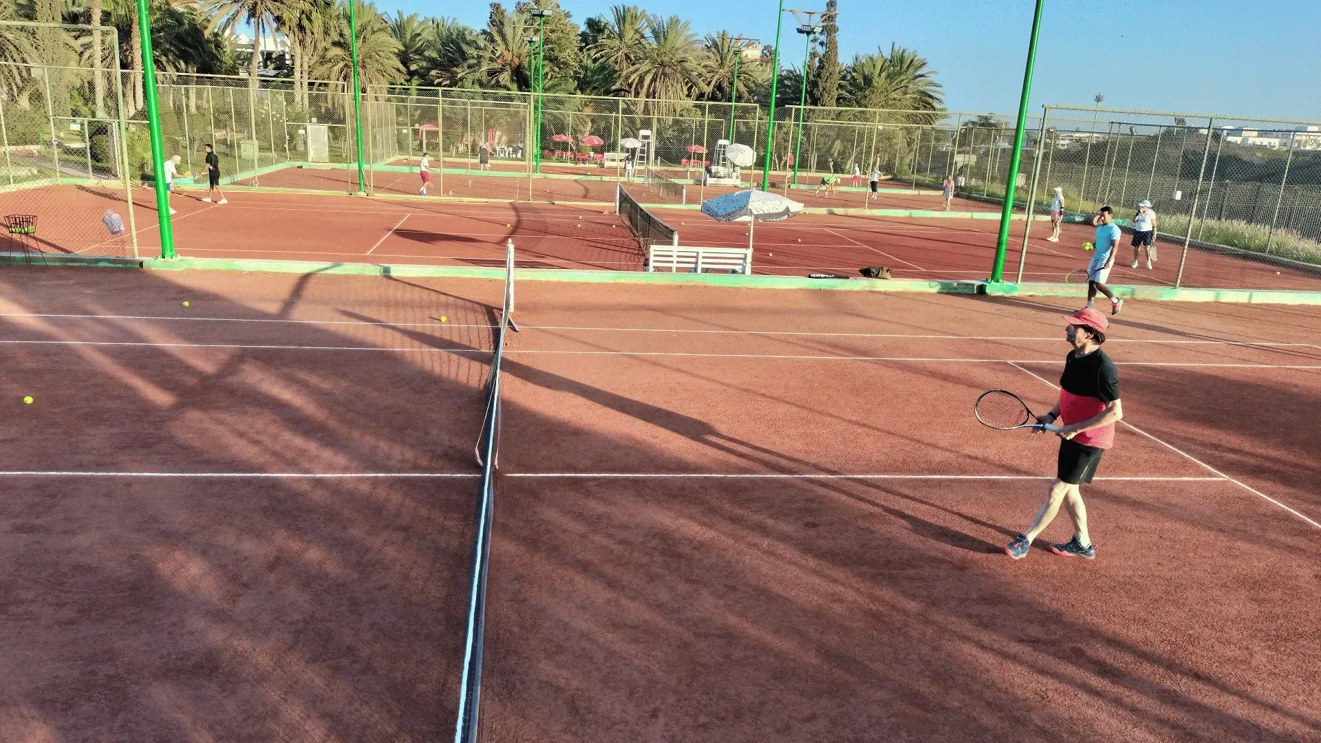 Terrains de tennis à louer à Agadir : vue d'ensemble des courts en terre battue du club, palmiers en arrière-plan