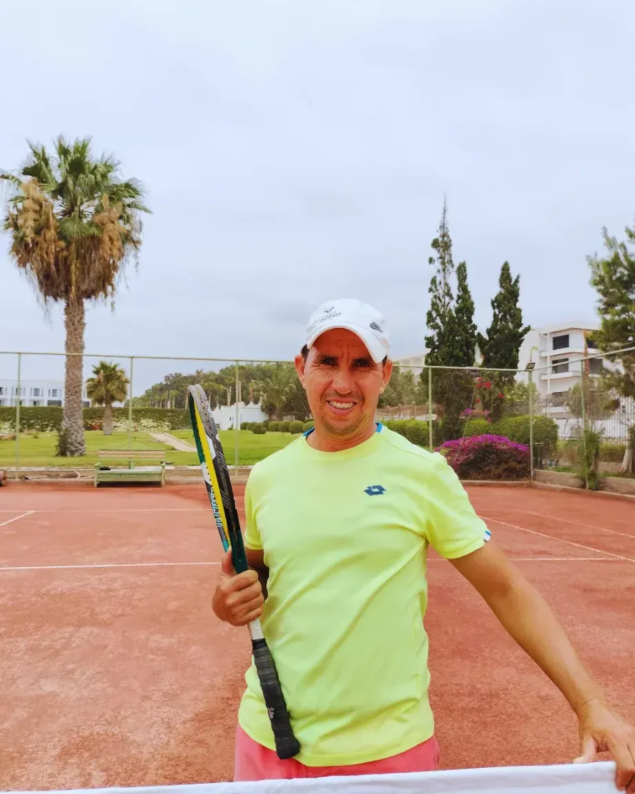 Le coach M.Mohamed, raquette à la main, devant les courts du club et les palmiers
