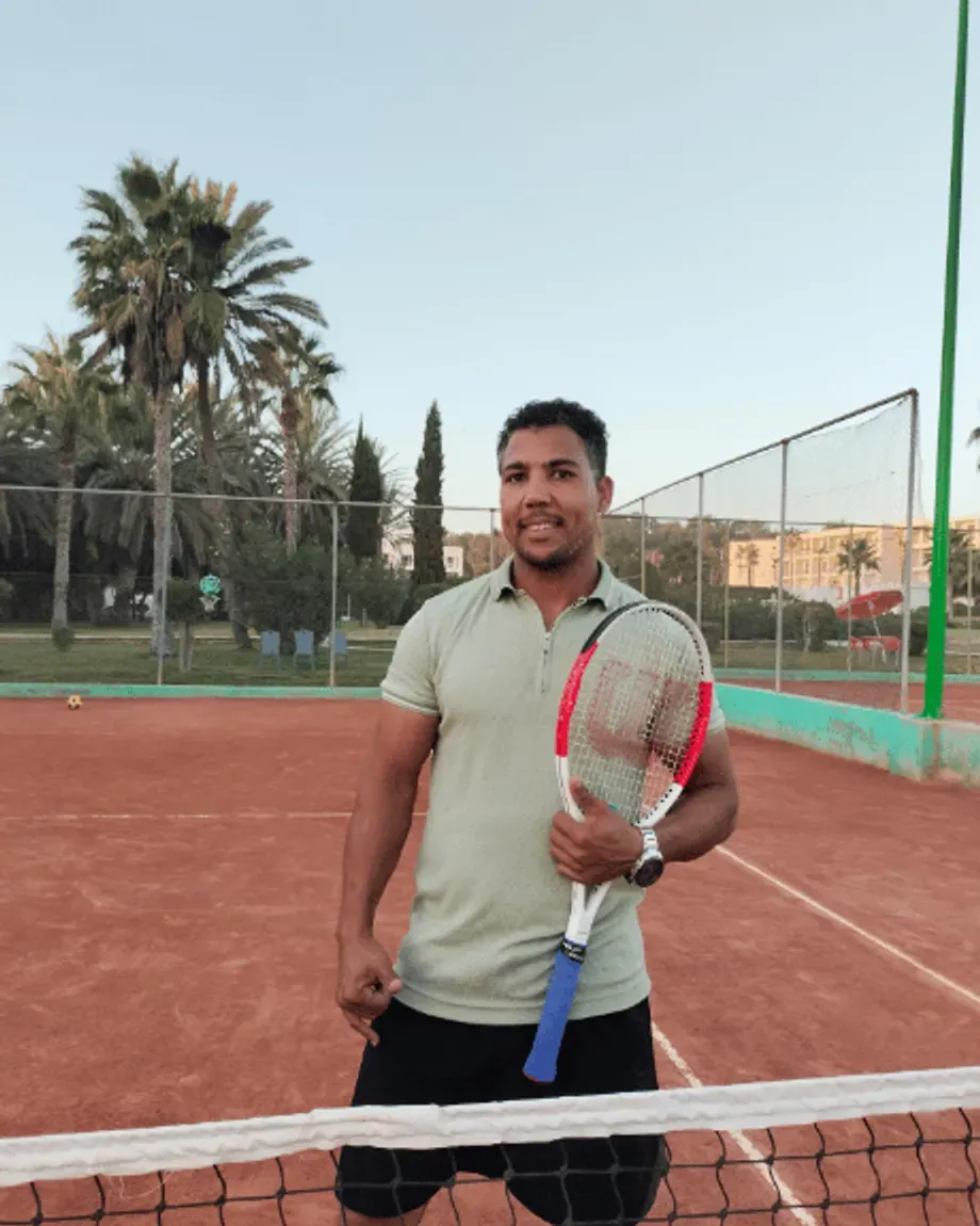 Le coach O.Khalid, raquette à la main, au filet sur un court en terre battue du club